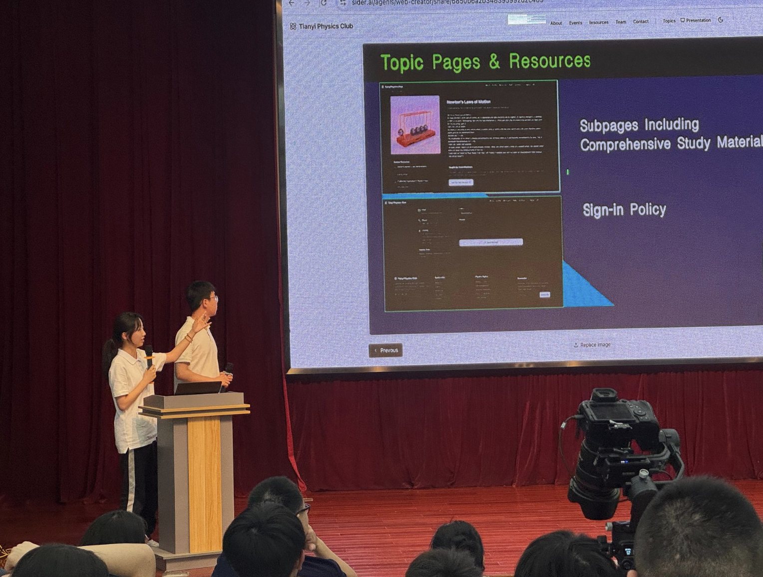 Two Physics Club officers presenting Topic Pages and Resources on stage, with study-material subpages shown on the screen behind the lectern